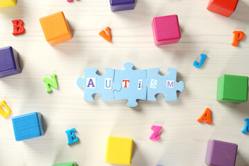 Word Autism made of puzzle pieces, colorful cubes and letters on white wooden table, flat lay