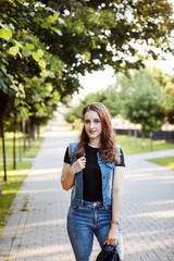 Portrait of young woman in casual clothes, black t-shirt, denim vest and jeans spending time in the park in summer.