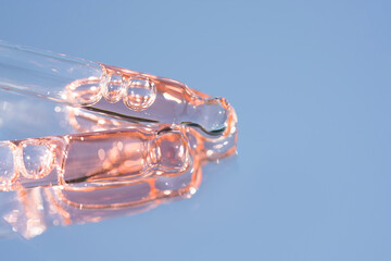 Two pipettes with pink liquid on blue glass background with copy space. Texture of face serum or...