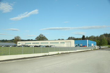 Fototapeta na wymiar Factory building with parking lot surrounded by fence on sunny day