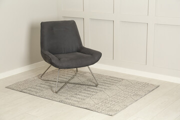 Stylish grey armchair near light wall in room. Space for text