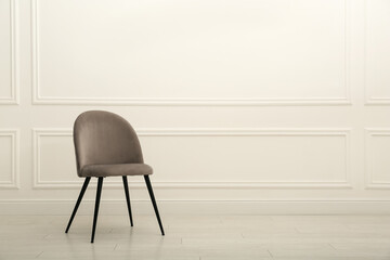 Modern beige chair near white wall indoors. Space for text