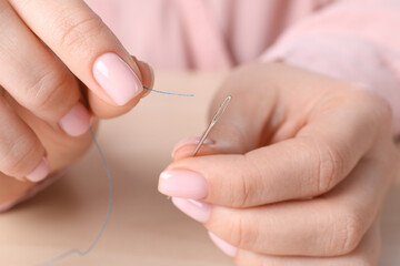 Woman threading sewing needle at table, closeup