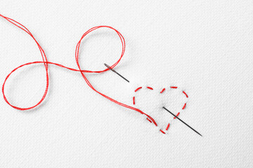 Needle with red thread and stitches in shape of heart on white fabric, top view