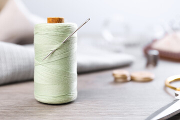 Spool of light green sewing thread with needle and scissors on wooden table, space for text