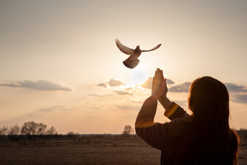 A woman prays a dove flies towards her as a symbol of hope for the peace.