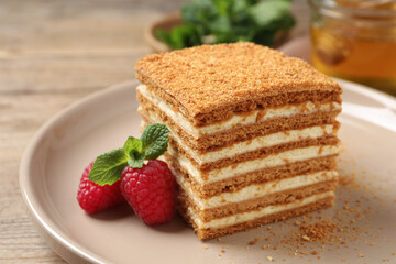 Slice of delicious layered honey cake served with mint and raspberries on plate, closeup