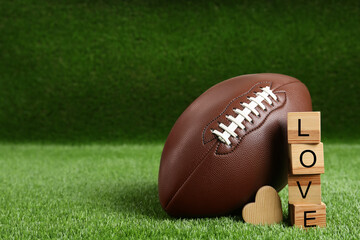 American football ball, cubes with word Love and heart on green grass. Space for text