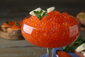 Cocktail glass of delicious red caviar with parsley and butter on table, closeup