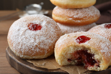 Delicious donuts with jelly and powdered sugar on wooden board, closeup