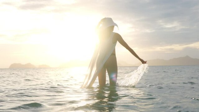 Woman In Thong Splashing Water In Sea Towards Glowing Sunset