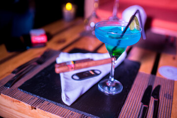 Closeup photo of many cigars on the table with a blue cocktail
