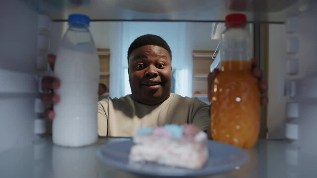 View From Fridge Of Cheerful Afro-american Man. Close-up Footage Of Smiling Guy Taking Cake, Closing Door At Night. Kitchen. Unhealthy Food Concept. Diet. Shooting Inside Of Refrigerator. Indoors