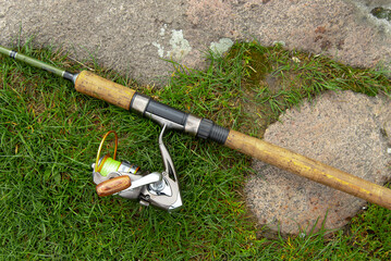 Fishing reel on a fishing rod that lies on the grass.
