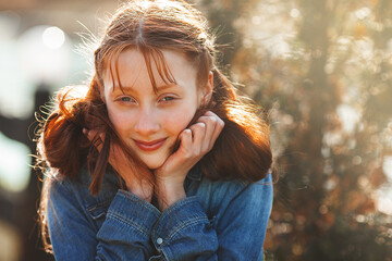 Pretty young red-haired girl outdoors. Teenager closeup portrait. Cheerful young girl outside in...