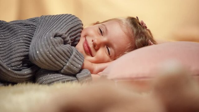 Portrait of relaxed smiling happy child falling asleep in tent in living room. Cute Caucasian carefree child closing eyes lying on soft carpet dreaming. Leisure and childhood concept