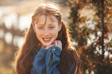 Pretty young red-haired girl outdoors. Teenager closeup portrait. Cheerful young girl outside in...