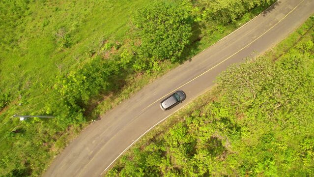 AERIAL TOP DOWN: Winding vehicle bypassing potholes while driving through exotic countryside. Gray car travelling along paved road in tropics avoiding asphalt holes. Damaged roads in third world.