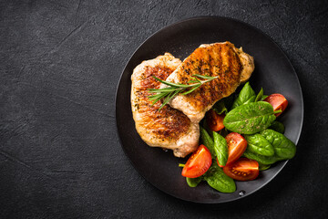 Meat steaks with fresh salad. Top view image at black table.