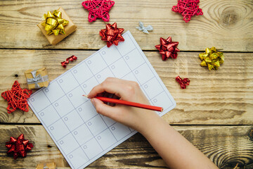 A Christmas composition with a glider or calendar, a woman's hand holding a pencil. Bows and gifts on a wooden background. The concept of Christmas and New Year.