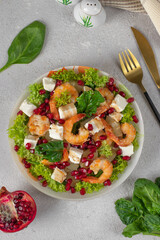 Salad with shrimps, pineapple, feta and pomegranate seeds in a plate on green lettuce leaves, on light gray background