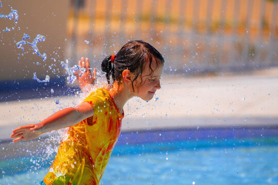 Young happy emotional child girl under a water stream outdoors at water park. Summer water park holiday and happy childhood concept. Copy space. Horizontal image.
