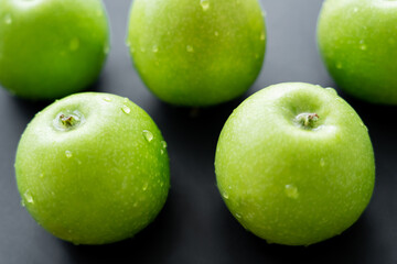 close up view of green and juicy apples with water drops on black.
