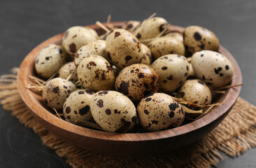 Bowl with quail eggs and straw on black table, closeup