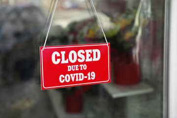 Fototapeta premium Red sign with text Closed Due To Covid-19 hanging on glass door. Coronavirus quarantine