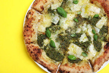 Delicious pizza with pesto, cheese and basil on yellow background, top view
