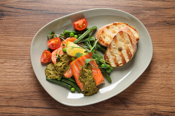 Tasty cooked salmon with pesto sauce on wooden table, top view