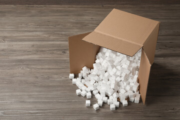 Overturned cardboard box with styrofoam cubes on wooden floor. Space for text