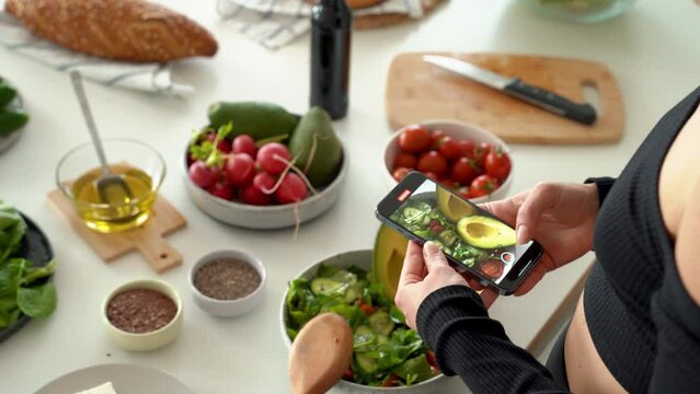 Closeup of female hands holding smartphone and taking pictures for social media in kitchen, cooking dietary meal from fresh vegetables in bowl. healthy eating concept. 4k footage