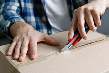 Man using utility knife to open parcel, closeup