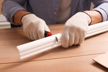 Man cutting foam crown molding with utility knife at wooden table, closeup