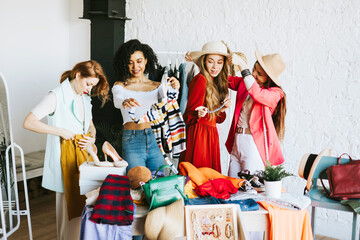 four young woman female caucasian and african students at swap party try on clothes, bags, shoes and accessories, change clothes with each other, second hand for things, zero waste life, eco-friendly