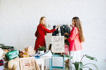 two young woman female caucasian students at swap party try on clothes, bags, shoes and accessories, change clothes with each other, second hand for things, zero waste life, eco-friendly