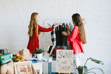 two young woman female caucasian students at swap party try on clothes, bags, shoes and...