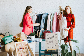 two young woman female caucasian students at swap party try on clothes, bags, shoes and...