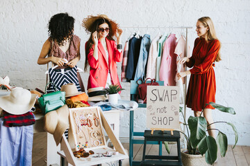 three young woman female caucasian and african students at swap party try on clothes, bags, shoes...