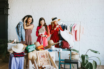 three young woman female caucasian and african students at swap party try on clothes, bags, shoes...