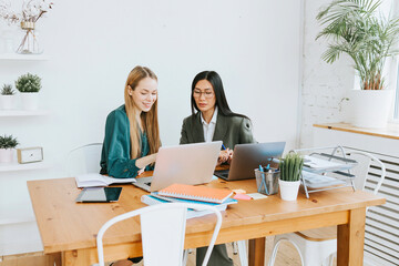 two young business women professionals in formal wear clothes work in modern office using laptop, tablet, brainstorm and search for solutions together, confident independent Asian girl solves problems