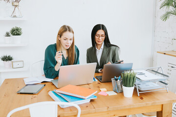 two young business women professionals in formal wear clothes work in modern office using laptop, tablet, brainstorm and search for solutions together, confident independent Asian girl solves problems