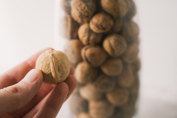 A man holds a walnut in his hand against the background of a glass vase with nuts.