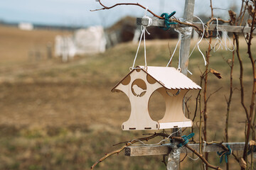 Wooden bird feeder on ropes with a blurred background on the field. House for birds.