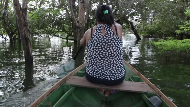 Young  native woman paddling a boat in a river igarape between trees in the Amazon Rainforest. Concept of travel, environment, ecology, tourism, conservation, people, ecology, climate change.