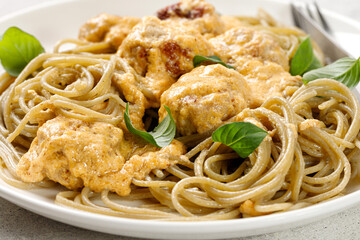 Cooked Whole grain pasta with meatballs with cream sauce and greens on white plate, grey background. Close up