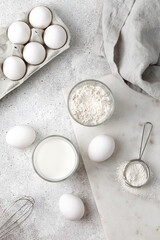 Dairy product. Milk, flour and eggs on grey background. Baking ingredients. White on white. Top view.
