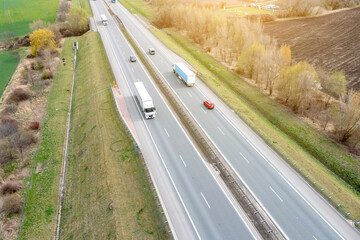 Many trucks are moving along the highway crossing road between the fields. drone view.