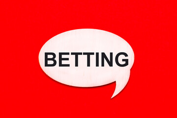 On a bright red background, a light wooden curly card with the text BETTING